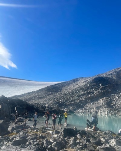 en gruppe mennesker som står på en steinete strand ved en vannmasse