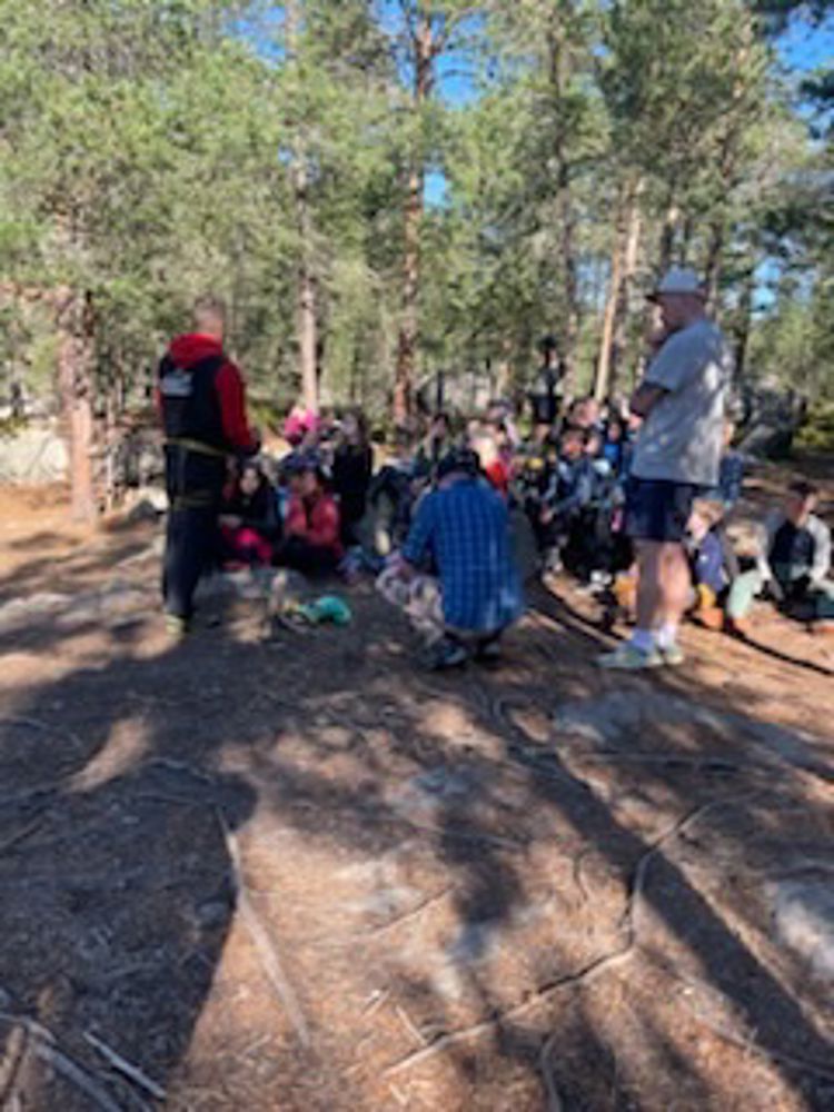 en gruppe mennesker som sitter på bakken foran trær