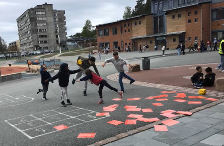 En gruppe mennesker som leker på en gårdsplass med bygninger i bakgrunnen